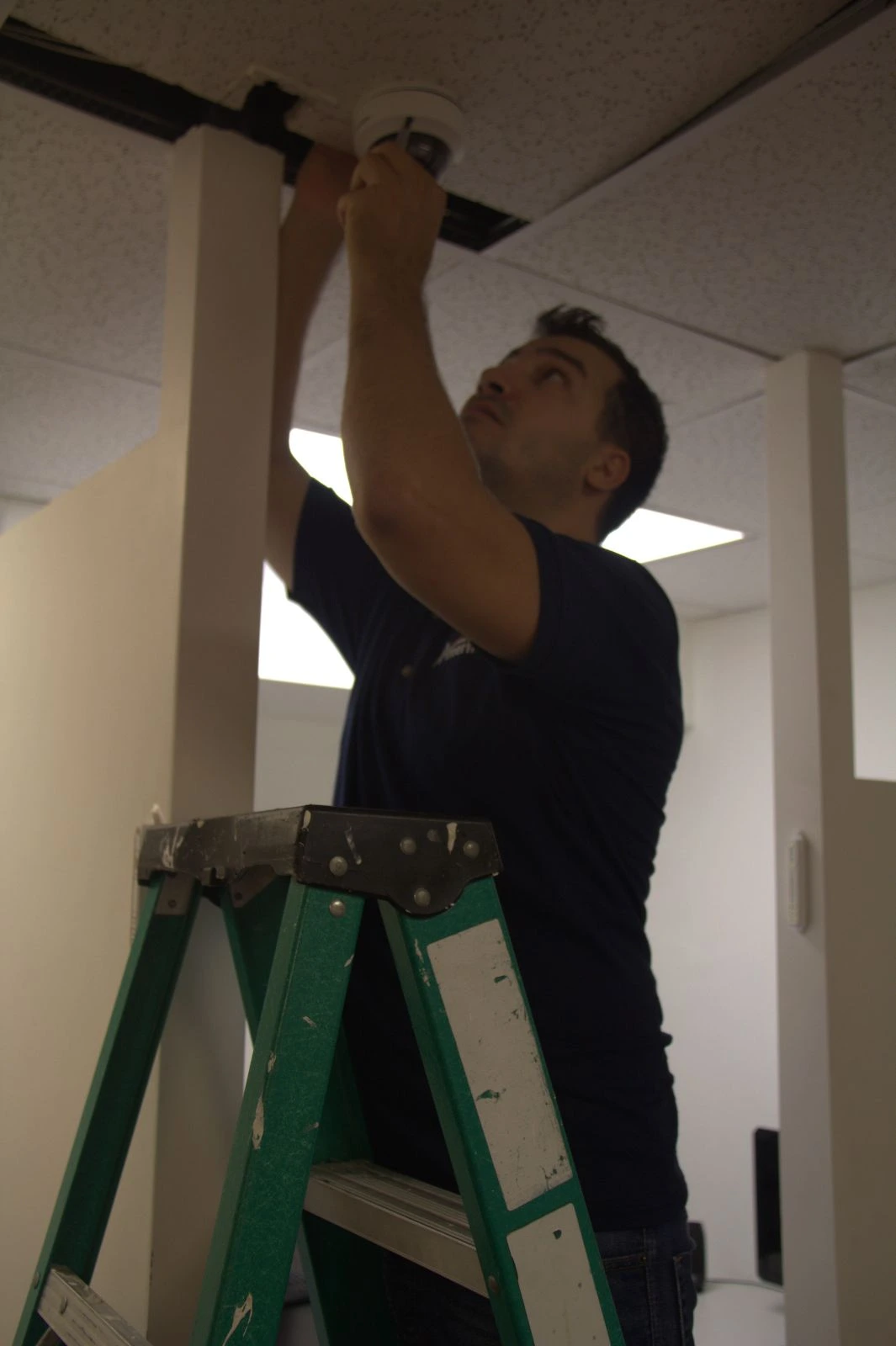 Local locksmith in Brooklyn installing ceiling-mounted CCTV security camera on ladder